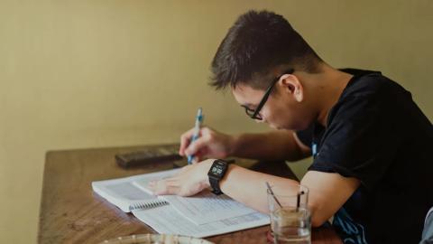 Mladý muž si dělá poznámky při studiu u stolu, ilustrace výběru MBA