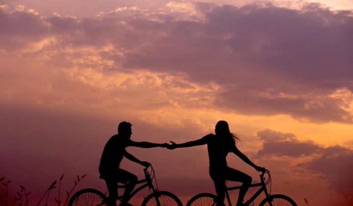 Zamilovaný pár na kolech se drží za ruce při západu Slunce