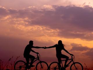 Zamilovaný pár na kolech se drží za ruce při západu Slunce